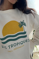Woman wearing white Les Tropiques sweater with retro sun and palm print, Bali-inspired design