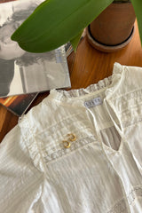 A flatlay of a frilled neck white top.
