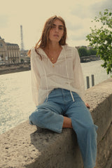 A woman sitting next to the river wearing white blouse and blue denim jeans