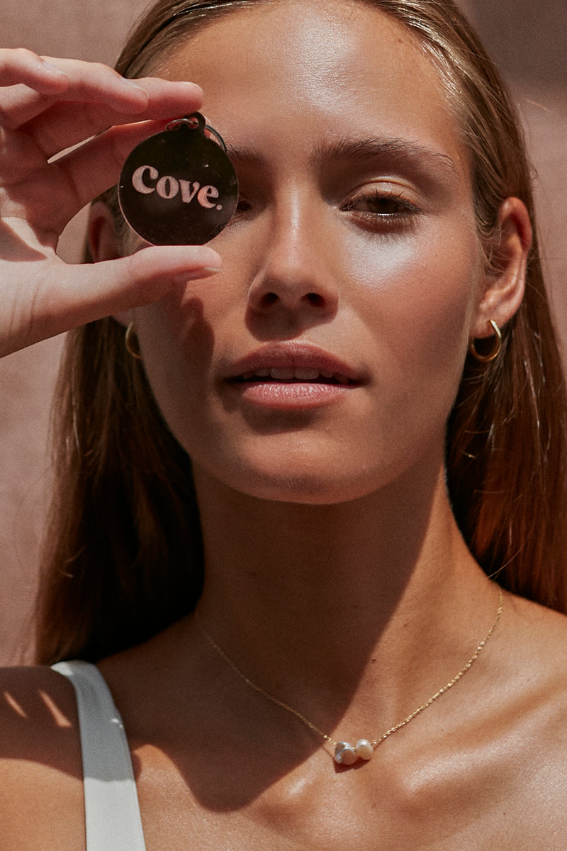 model holding a keyring with logo cove. island essentials in mirror effects