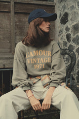 A green women's crew neck sweater styled with white pants and cap