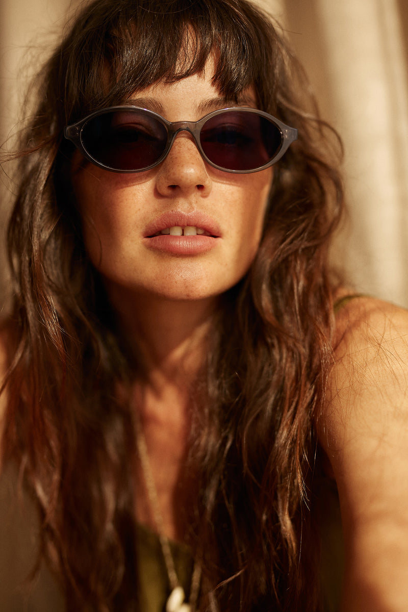A woman wearing cove sunglasses in Crystal Grey with Grey Lens by Maison Mata