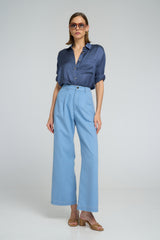 Model wears the LILYA draped blue blouse worn with casual wide-leg chambray pants.