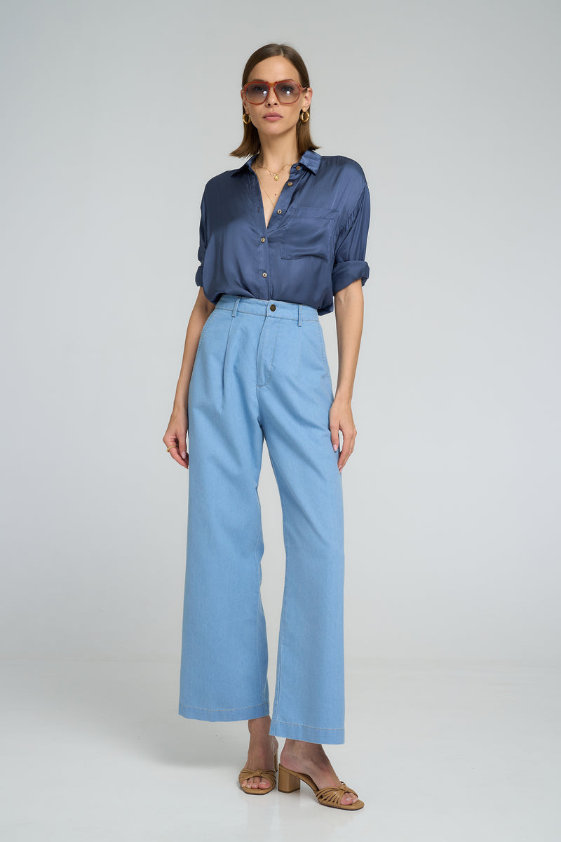Model wears the LILYA draped blue blouse worn with casual wide-leg chambray pants.