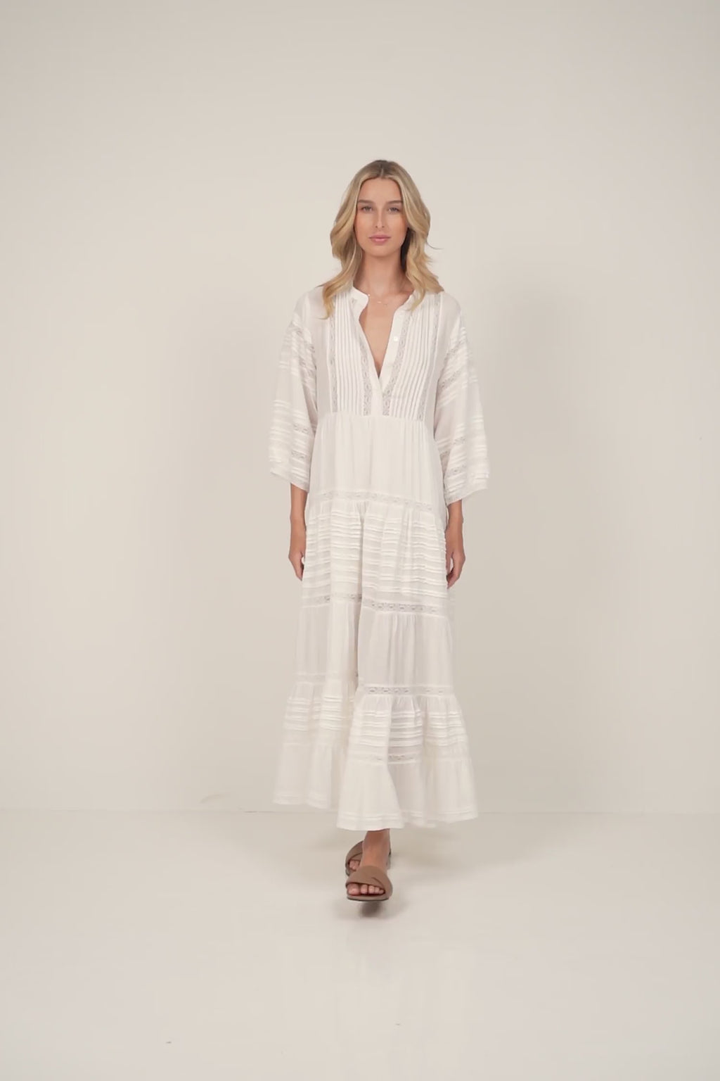 A model wearing a white maxi dress with lace and pleat details