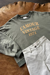 A flat lay of womens collegiate style logo crew neck sweater with white pants